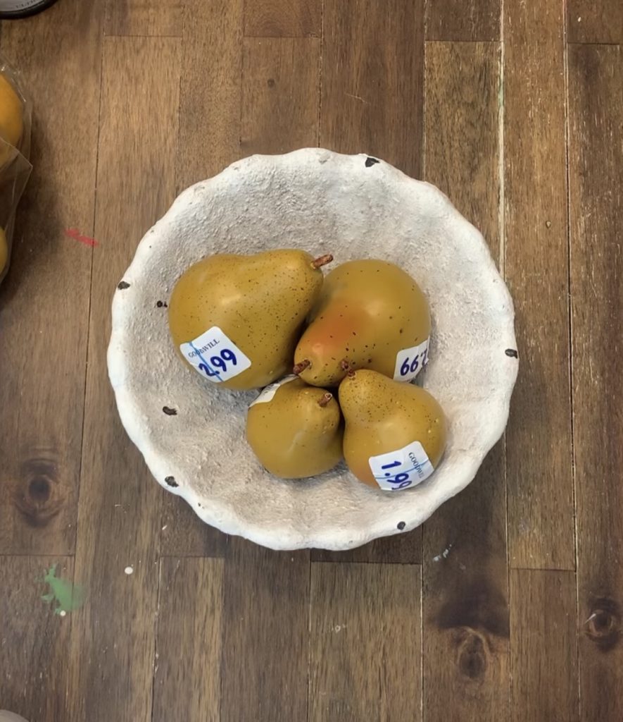 Four faux pears with Goodwill stickers sit in a cement bowl.