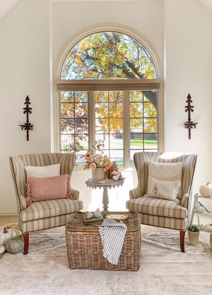 Two striped wingback chairs sit in front of an arch interior window in a French Cottage living room. Pumpkins, fall florals and pears are sprinkled throughout the room.