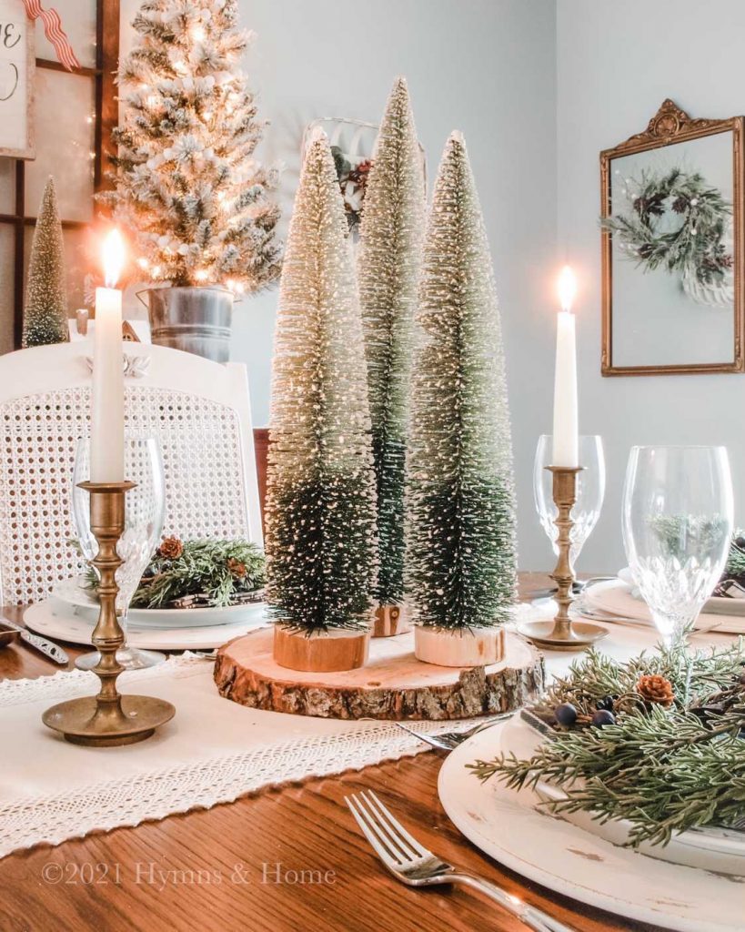 Three tall bottle brush trees sitting on top of a wood charger create a centerpiece on a Christmas dining table