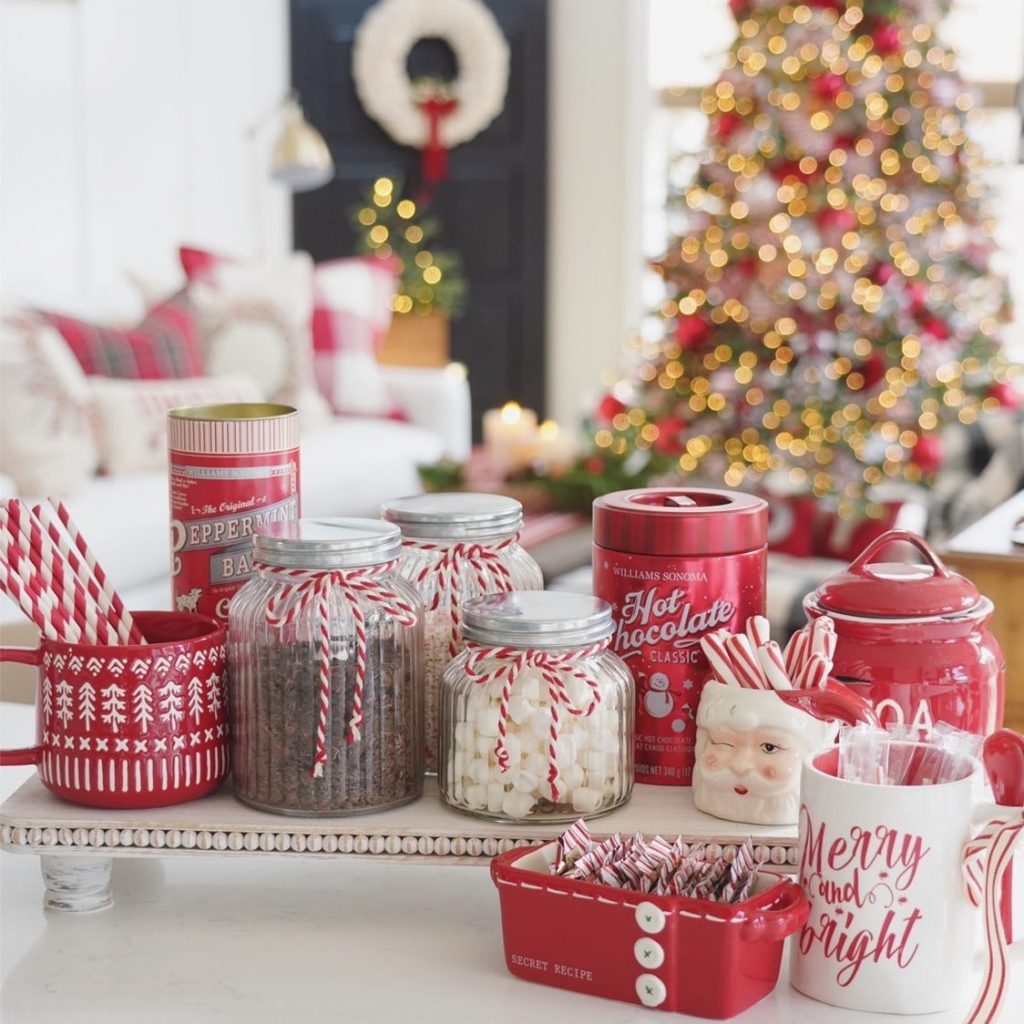 Red tins, clear glass jars tied with red & white string and Christmas mugs sit on a counter.