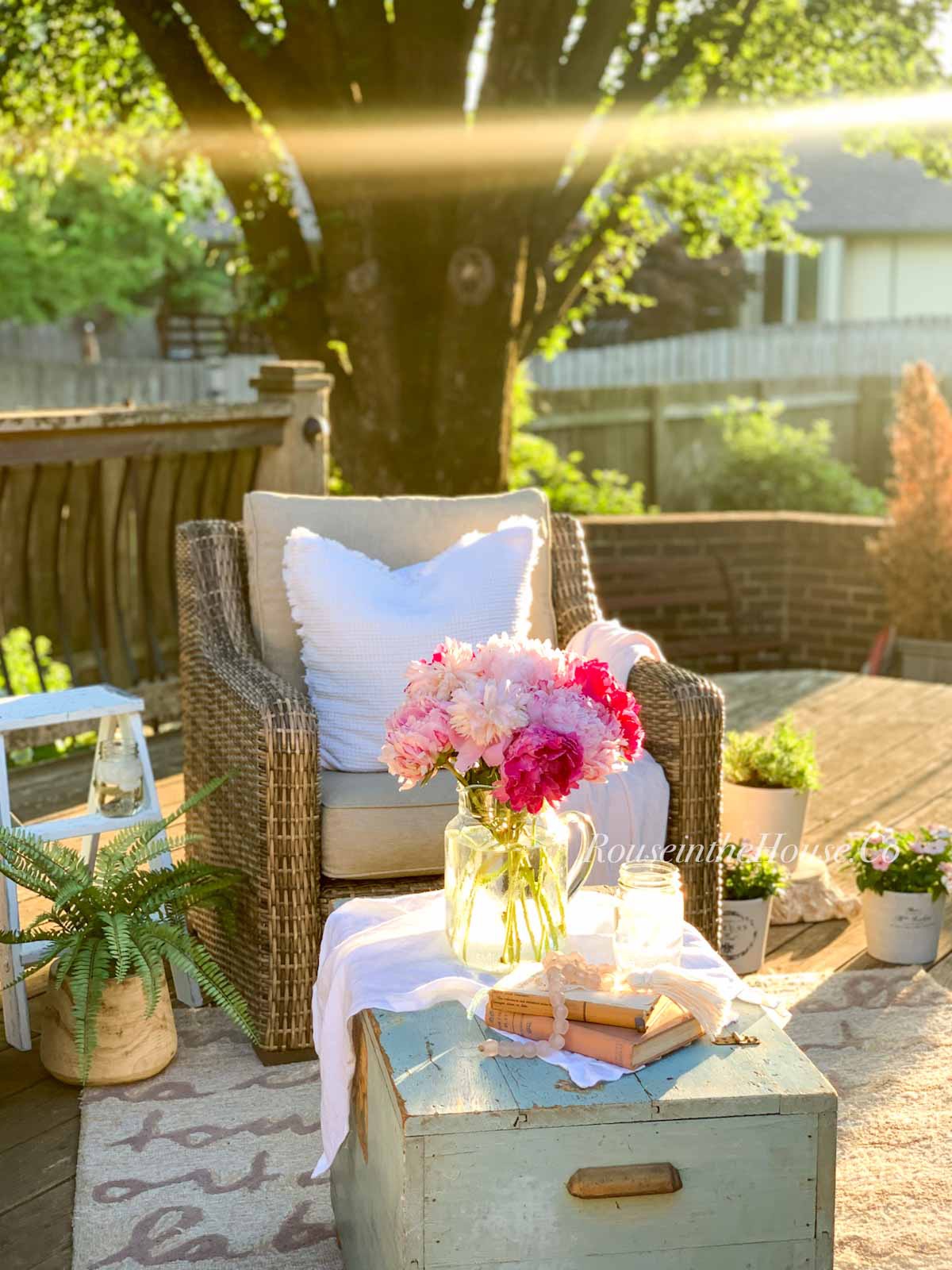 a DIY painted plant stand stenciled in a French Blue French Script is sitting on an outdoor patio. A small vase of pink peonies sit on top of a vintage chest.