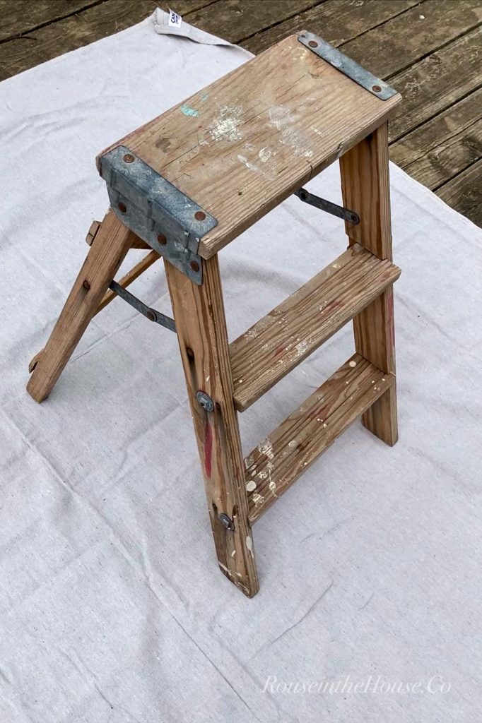 An old step ladder sitting on a drop cloth outside.