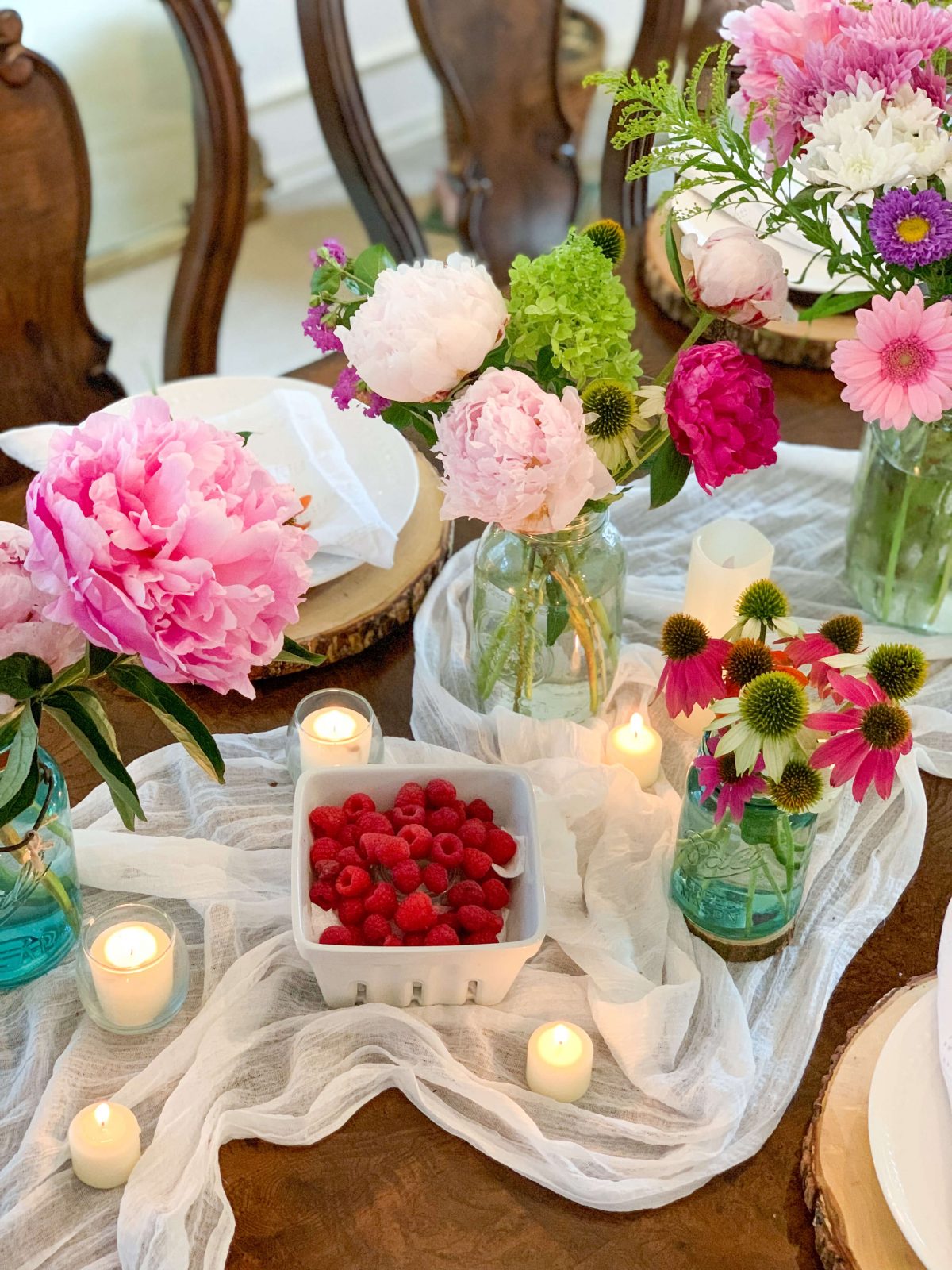 Red raspberries in a berry crate sit next to mason jar flower arrangements, lit candles and rustic place settings.