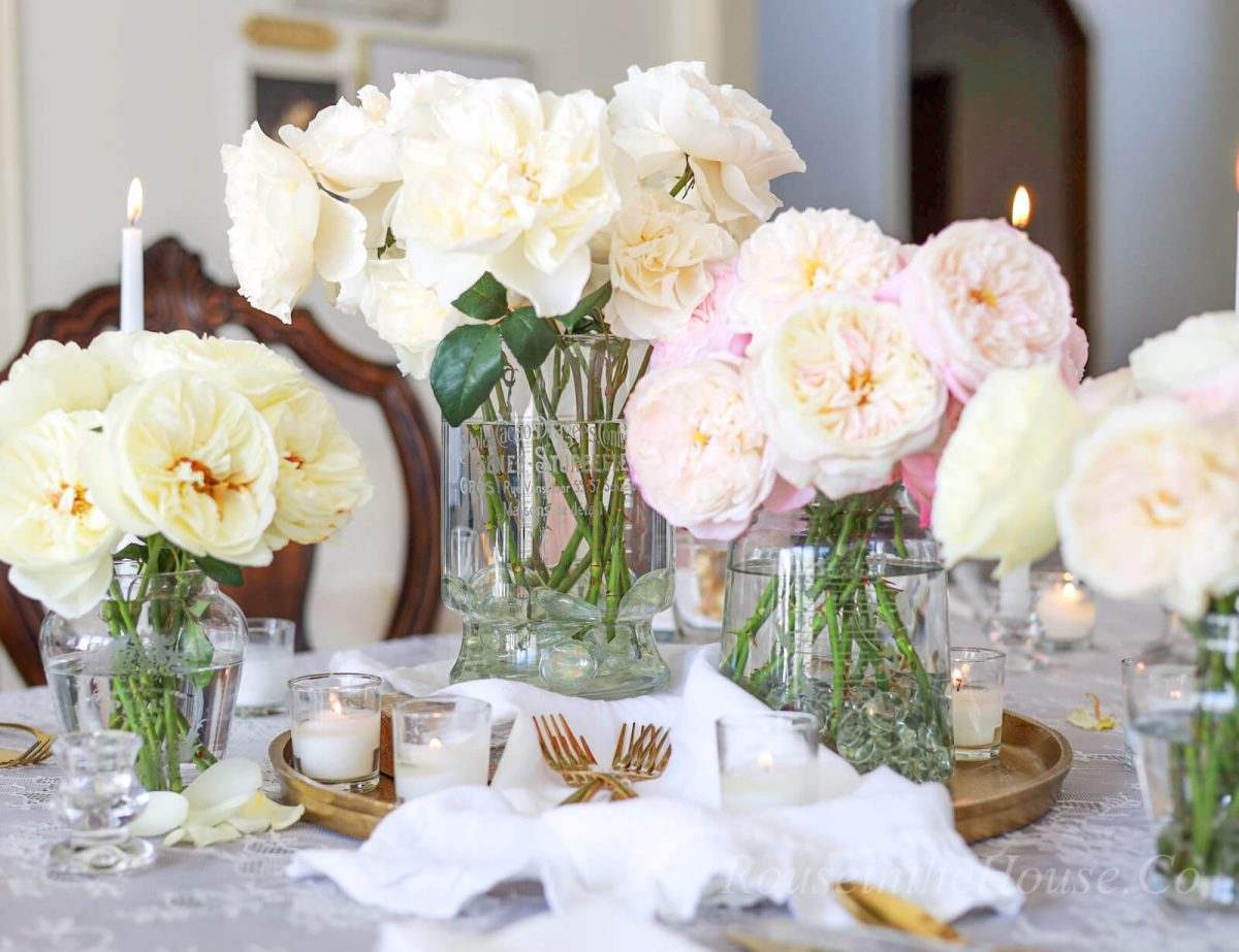 David Austin roses in etched flower vases make an elegant centerpiece. A tea towel is placed in front of them, where gold utensils rest.